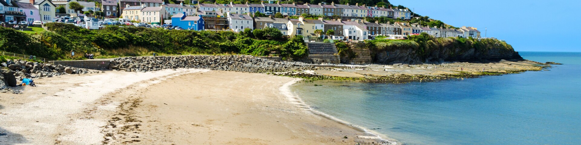 Un pueblo costero con casas coloridas en una colina, una playa de arena y un litoral rocoso.