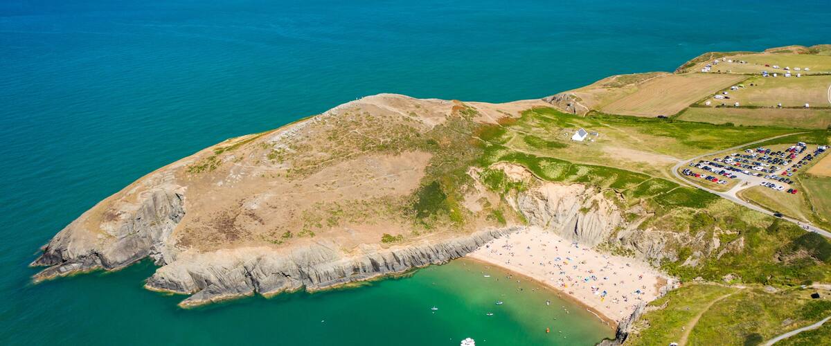 Un promontorio costiero con una spiaggia, un’area di parcheggio e una piccola barca in acqua.
