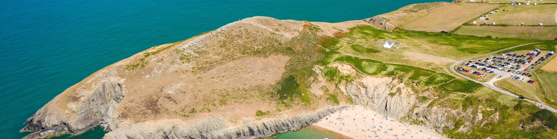 A coastal cliff with a beach, a parking area, and a small boat in the water.