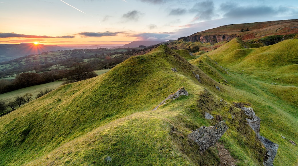 Des collines verdoyantes à perte de vue, un coucher de soleil et une ville lointaine.
