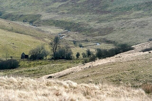 A winding river through a hilly landscape with sparse vegetation and a small house in the distance.