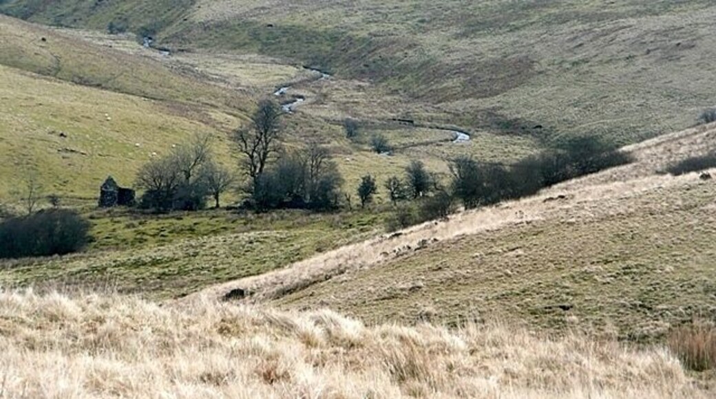 A winding river through a hilly landscape with sparse vegetation and a small house in the distance.