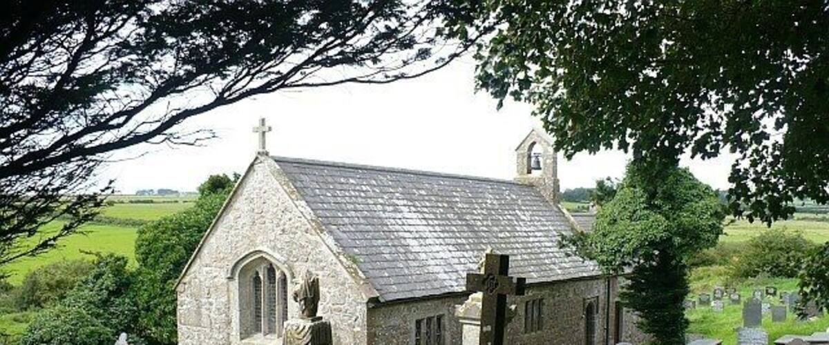 Una pequeña iglesia de piedra con un campanario, rodeada por un cementerio de lápidas.