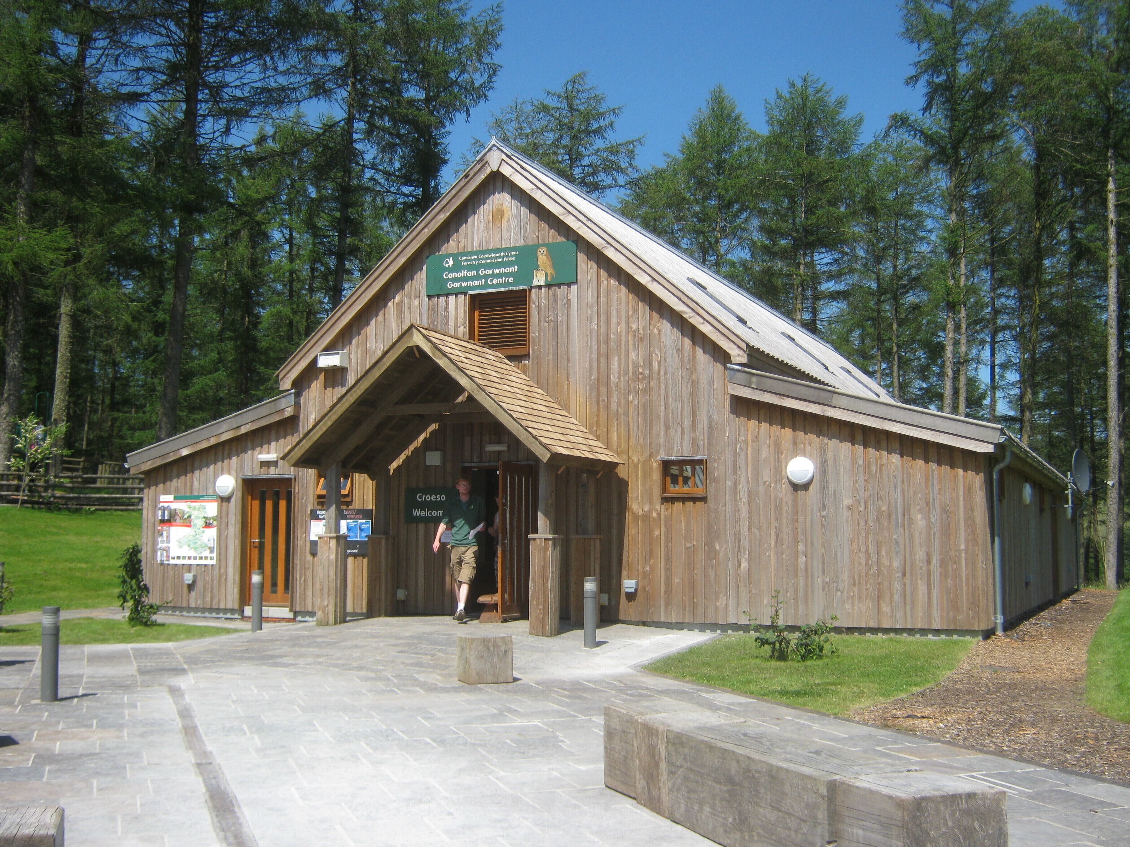 A wooden building with a sign reading "Canolaf Garwnant Centre" and "Croeso Welcor".