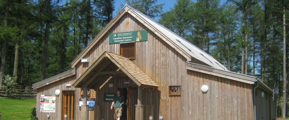 A wooden building with a sign reading "Canolaf Garwnant Centre" and "Croeso Welcor".
