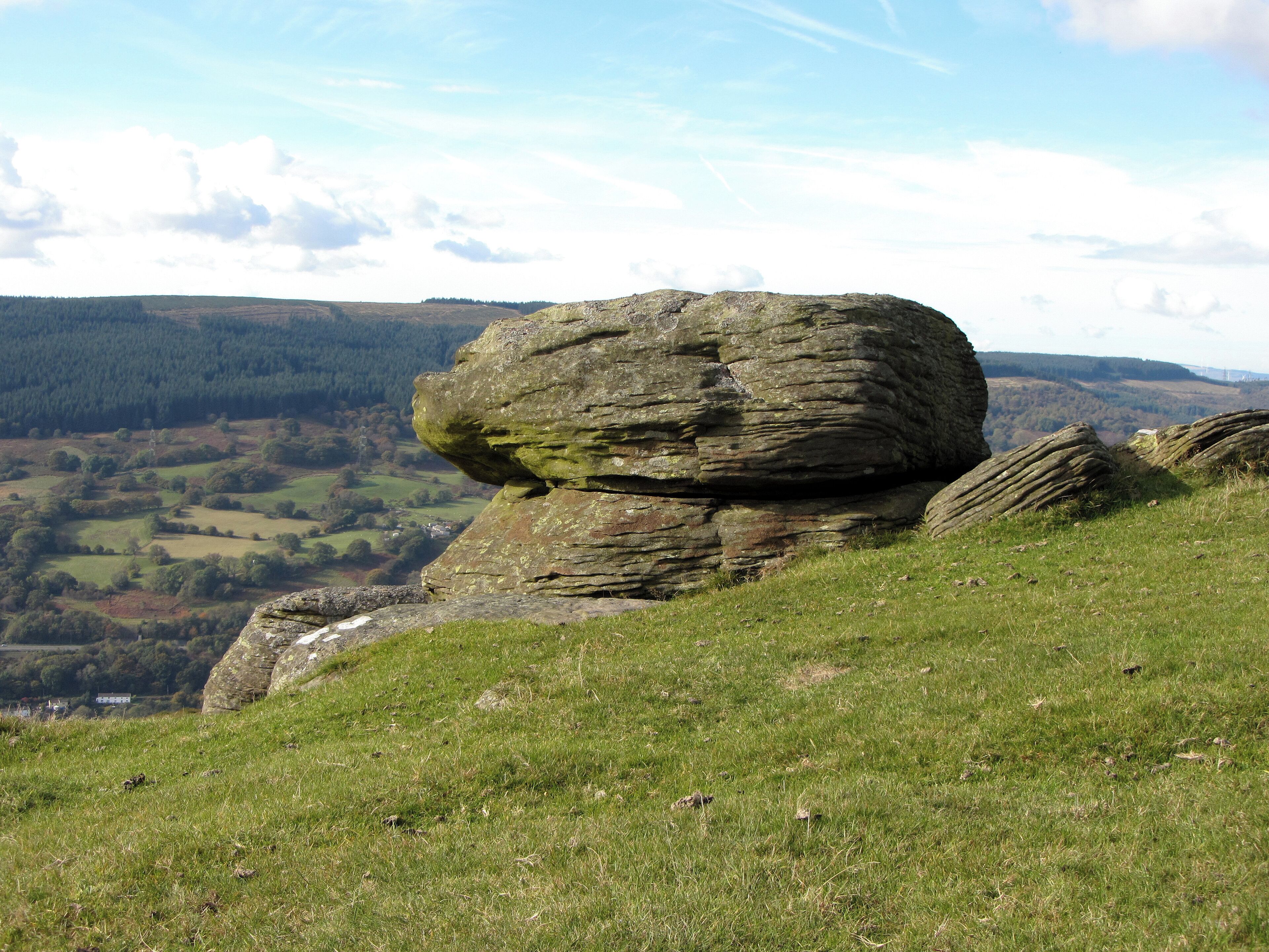 A large rock formation in a grassy field with a valley in the background.