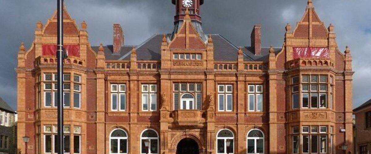 Een groot, versierd bakstenen gebouw met een opvallende klokkentoren, gebogen ramen en een centrale ingang.