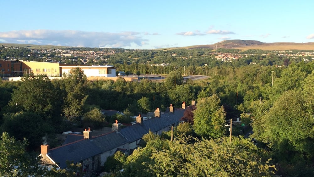 A rural landscape with scattered houses, dense greenery, and distant hills under a clear sky.