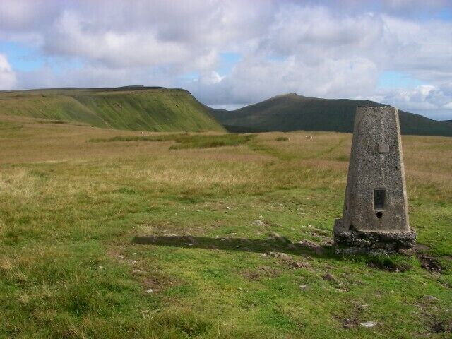 A stone cairn in a grassy field with rolling hills in the background.