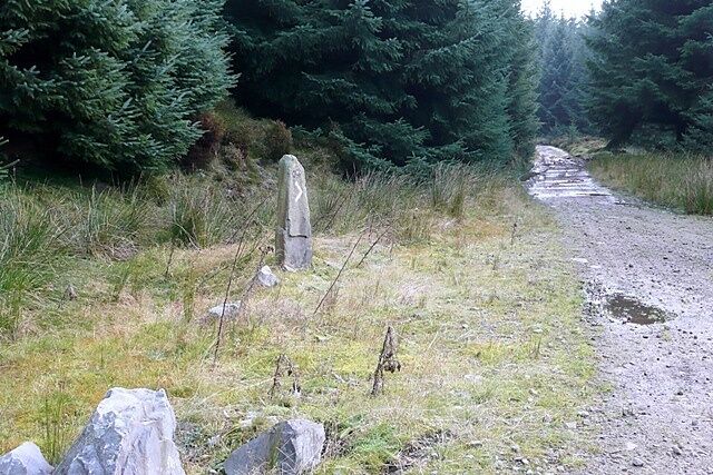 A gravel path with a stone monument and large boulders in a forested area.