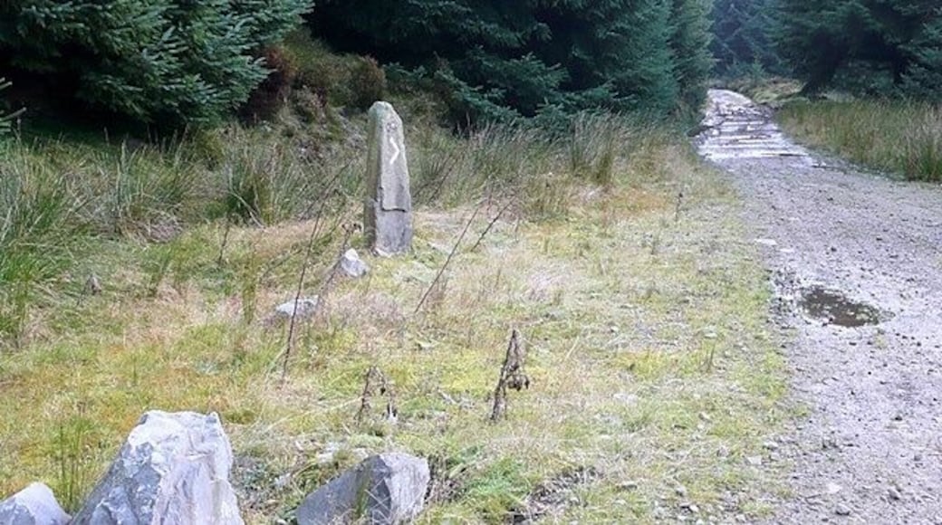 A gravel path with a stone monument and large boulders in a forested area.