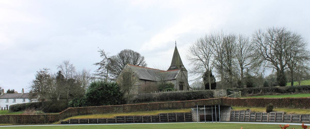 A church with a pointed steeple, surrounded by a grassy field and trees.