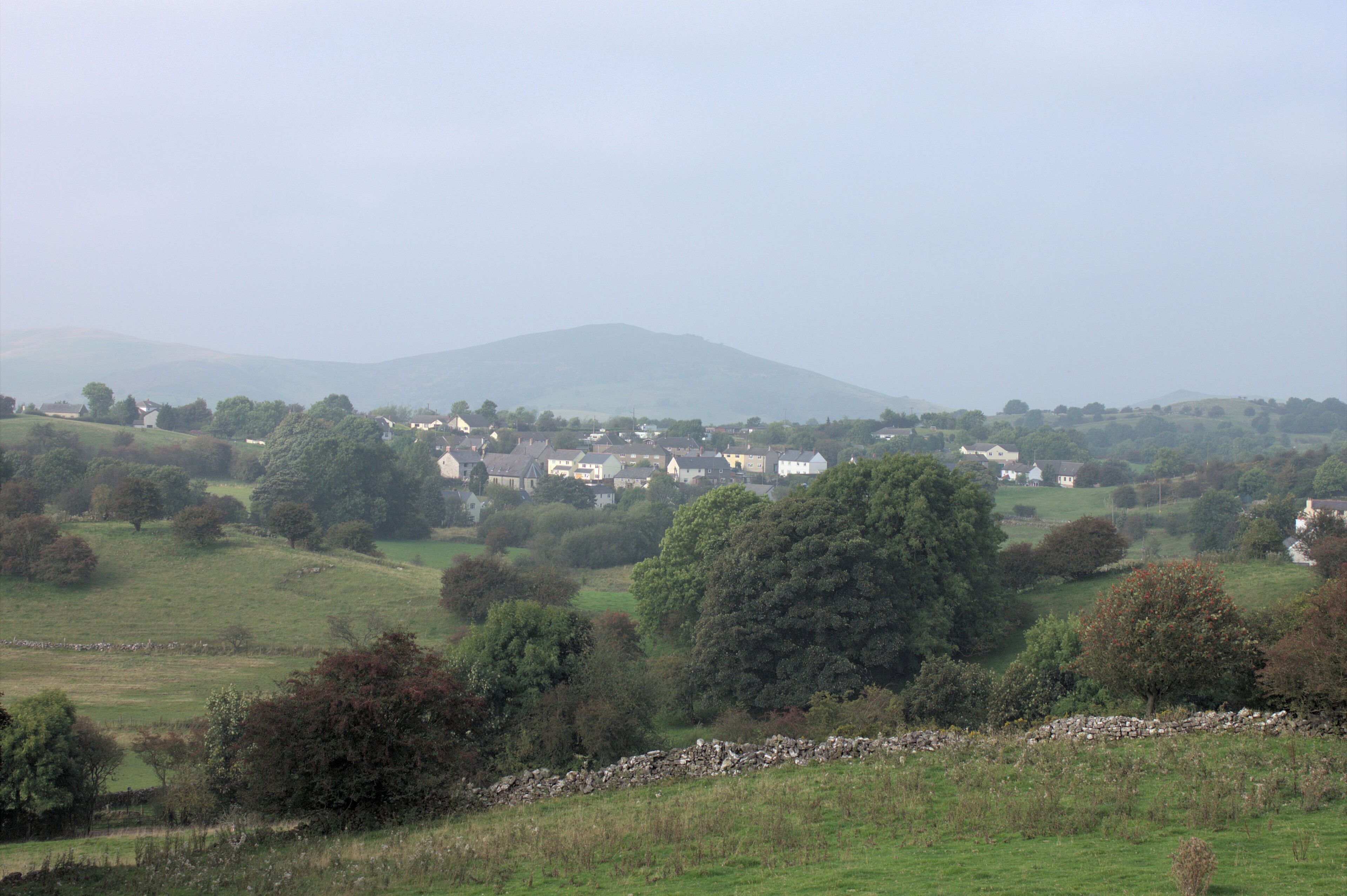 A rural landscape with rolling hills, scattered trees, and a village with white houses.
