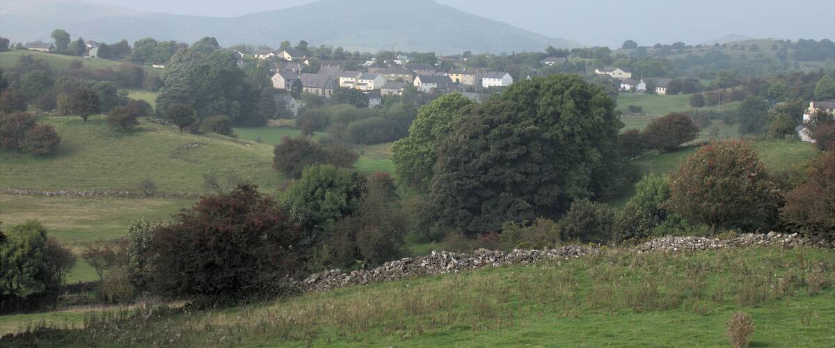 A rural landscape with rolling hills, scattered trees, and a village with white houses.