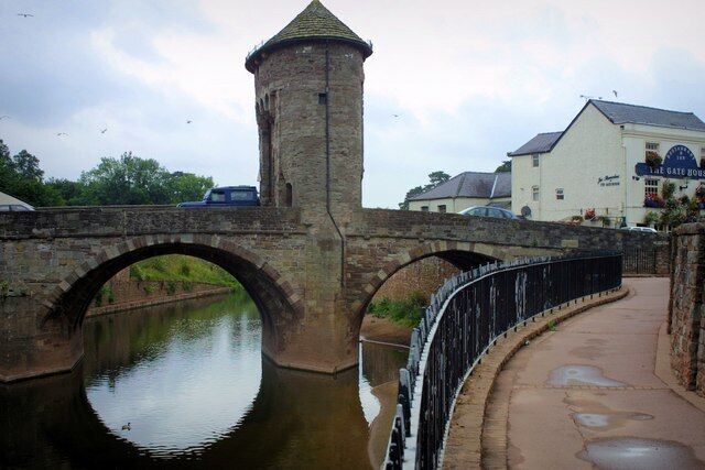 A stone bridge with a tower, a canal, and a building with a sign.
