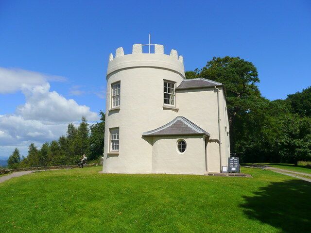 A white tower with a cross on top, surrounded by green grass and trees.