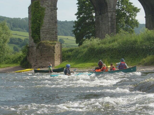 A group of people kayaking under a stone bridge with greenery around.