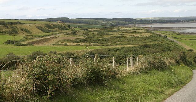 A rural landscape with rolling hills, a fence, and a body of water in the distance.