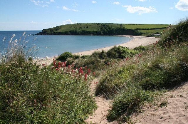 A coastal landscape with a sandy beach, green hills, and a clear blue sky.