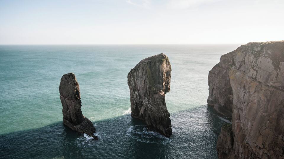 A coastal scene with three prominent rock formations in the sea.