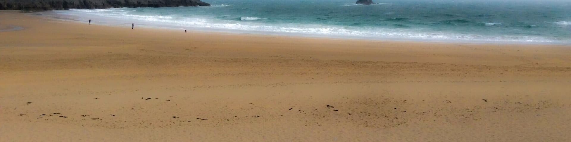 Una playa arenosa con olas suaves y un promontorio rocoso a lo lejos.