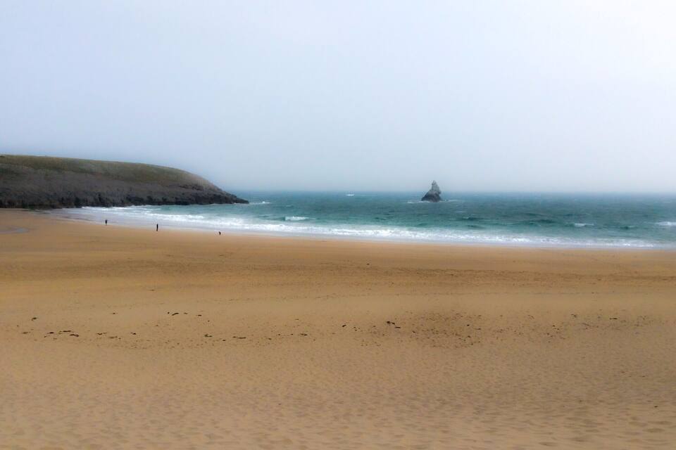 Une plage de sable fin, avec de douces vagues et un promontoire rocheux à l’horizon.