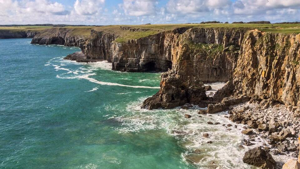 A coastal cliff with clear turquoise waters and a grassy landscape.