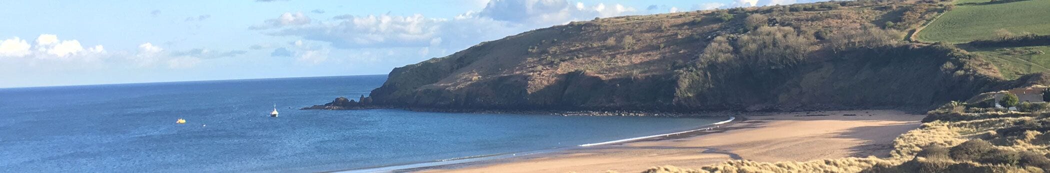 Paisagem costeira com uma praia arenosa, um penhasco rochoso e o oceano.