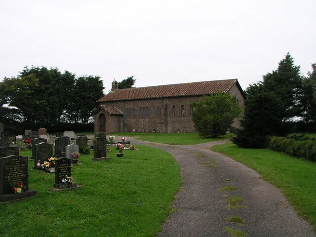 A church with a graveyard in front, surrounded by trees.