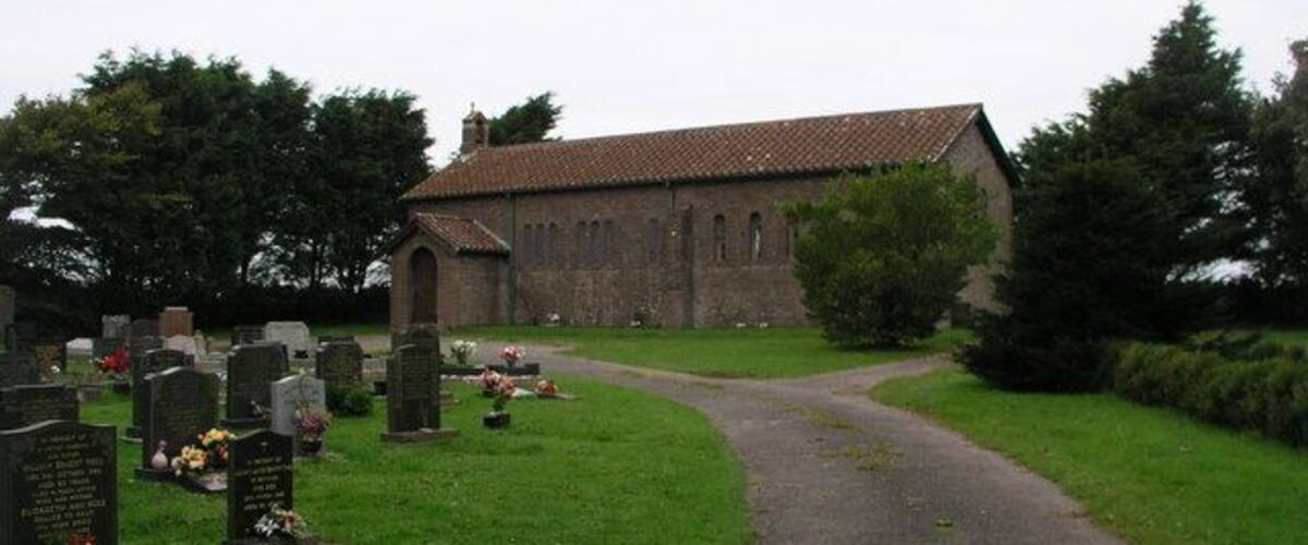 A church with a graveyard in front, surrounded by trees.