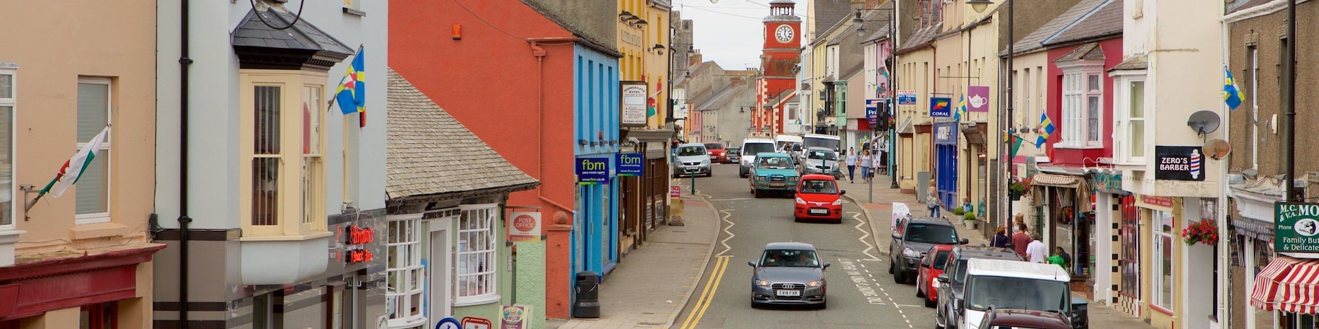 A street lined with colorful buildings, parked cars, and a clock tower in the distance.