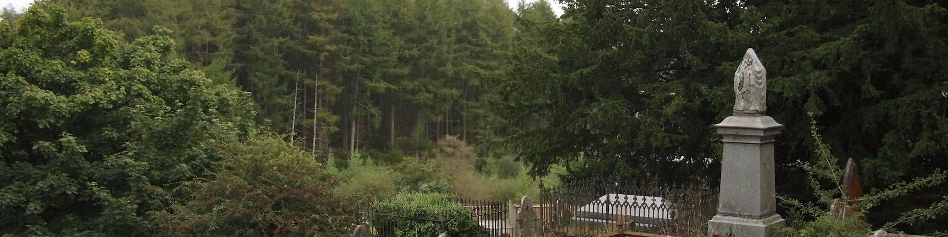 A cemetery with headstones, a stone monument, and a fence.