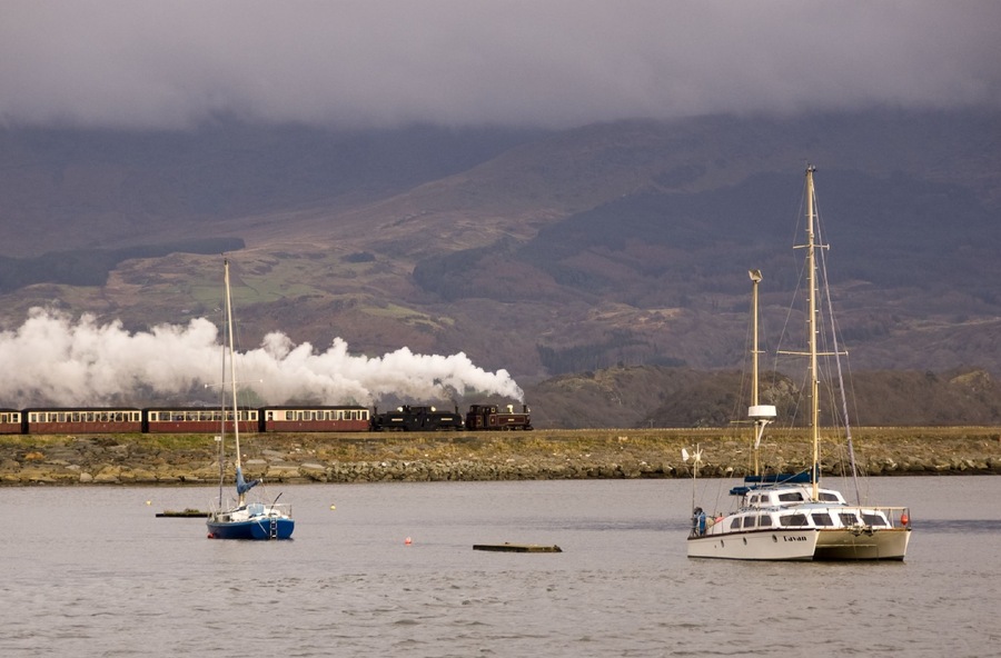 A Ffestiniog Railway train hauled by Earl of Merioneth and Taliesin heads across the Cob on its way to Blaenau Ffestiniog.