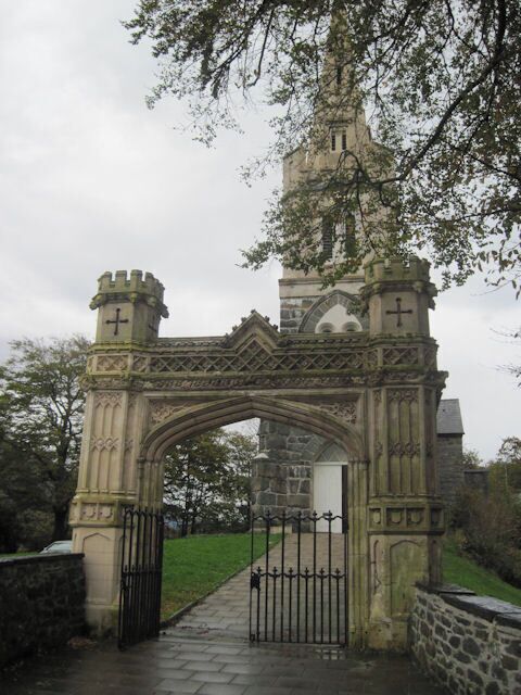 A stone archway with a tower and a clock, leading to a building.