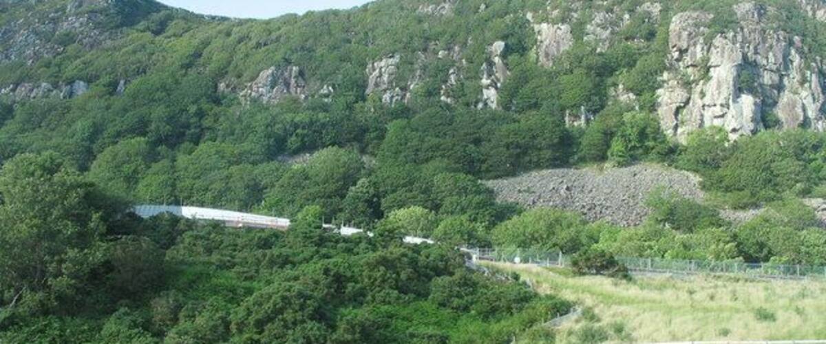 A mountainous landscape with dense greenery, rocky cliffs, and a building partially obscured by trees.