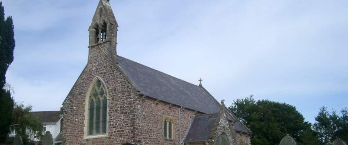 A historic church with a stone wall in front, surrounded by gravestones.