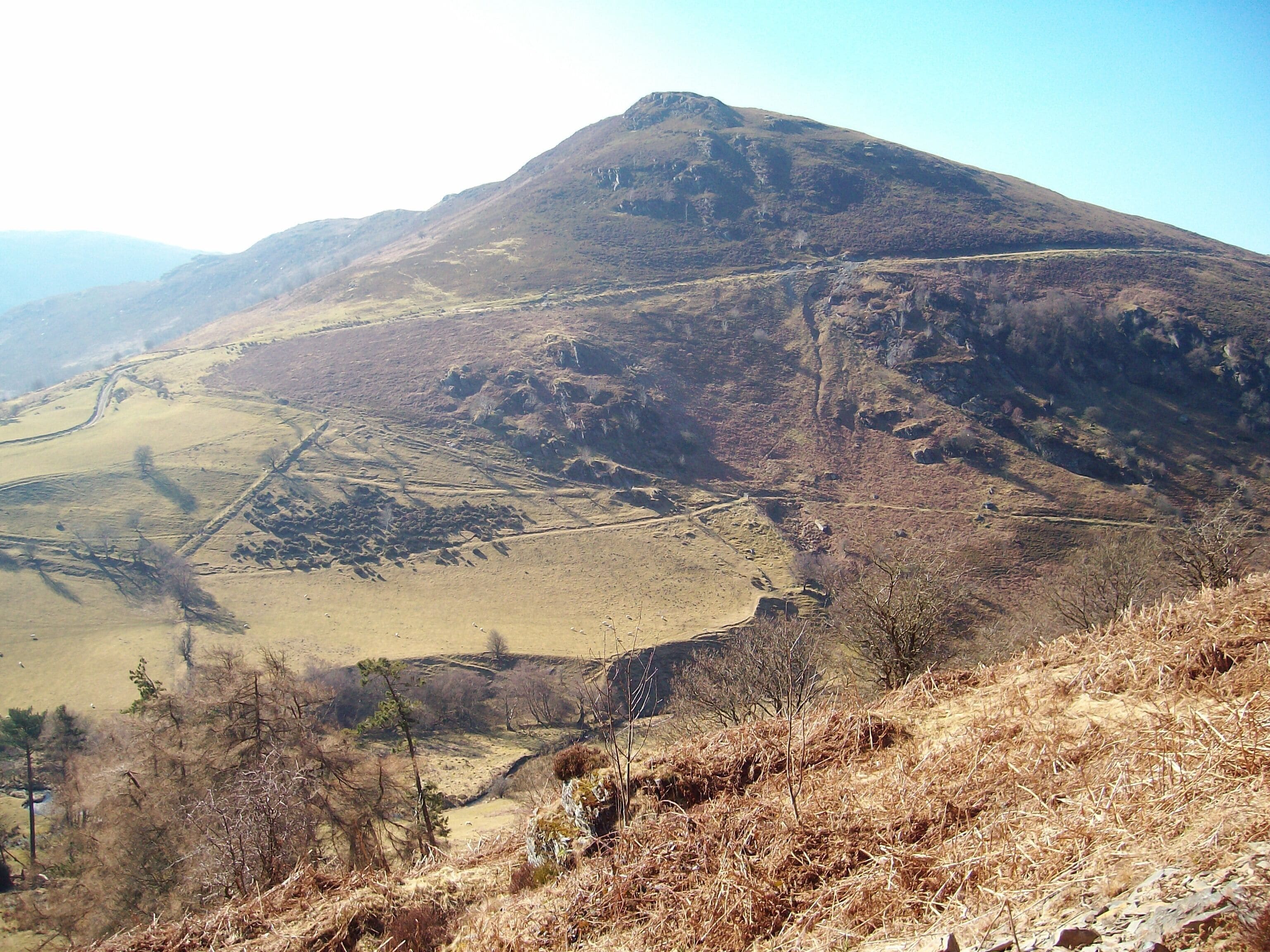 A mountainous landscape with a prominent peak, a valley, and a winding road.
