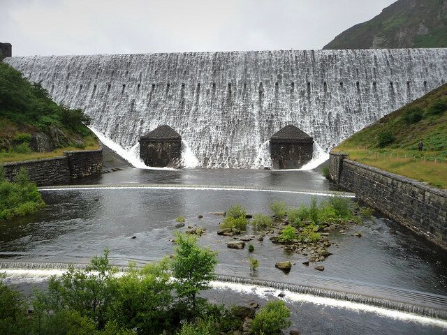 A dam with water cascading down, surrounded by greenery and rocky terrain.