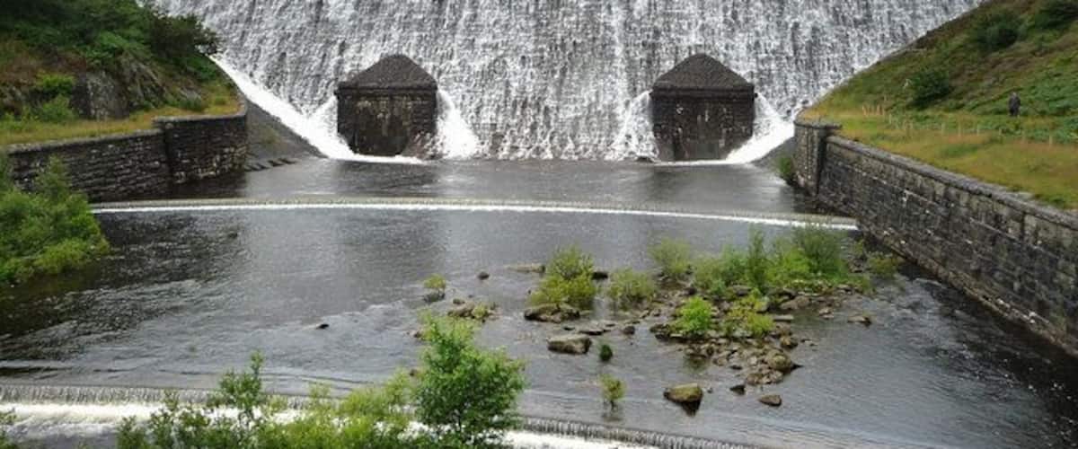 Una presa con agua cayendo en cascada, rodeada de vegetación y terreno rocoso.