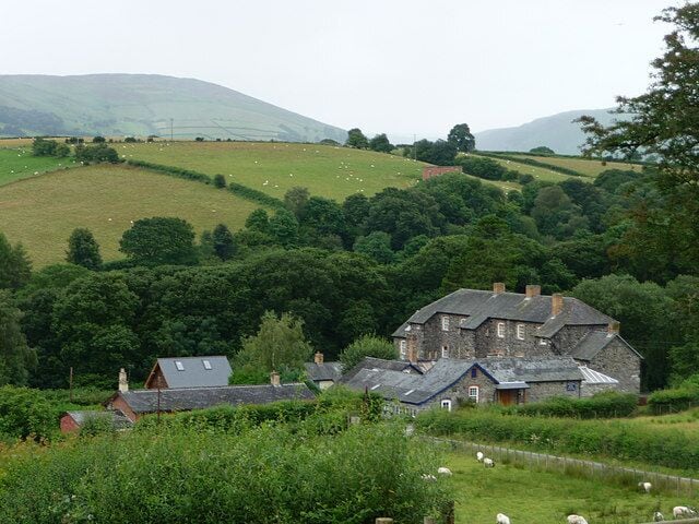 Eine ländliche Landschaft mit einem Steinhaus, umgeben von üppigem Grün und weidenden Schafen.
