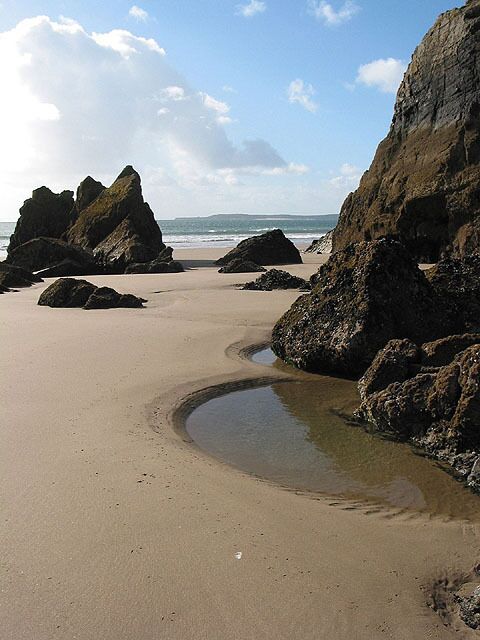 A sandy beach with large rocks and a small water channel.
