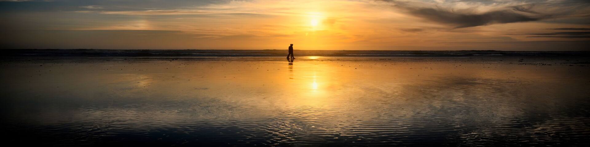 Couple walking on Freshwater West beach at sunset in Pembrokeshire, Wales