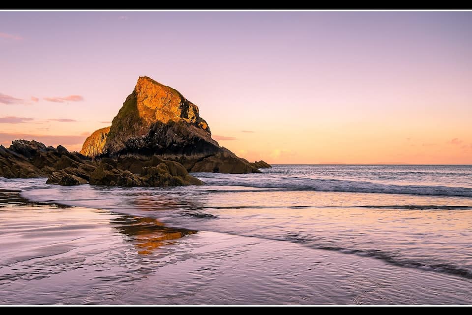Une côte rocheuse avec une falaise imposante, le tout baigné par les couleurs du coucher de soleil.