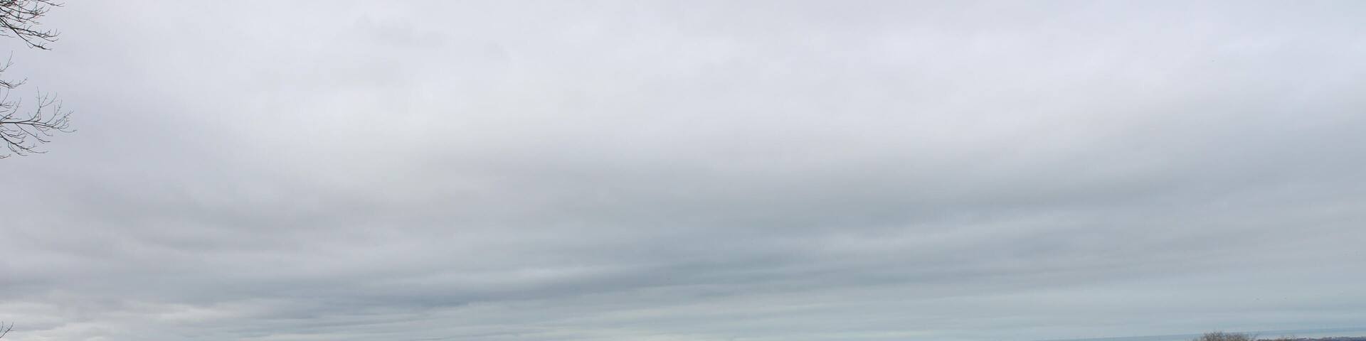 A rural landscape with rolling hills, scattered trees, and a distant view of a valley.
