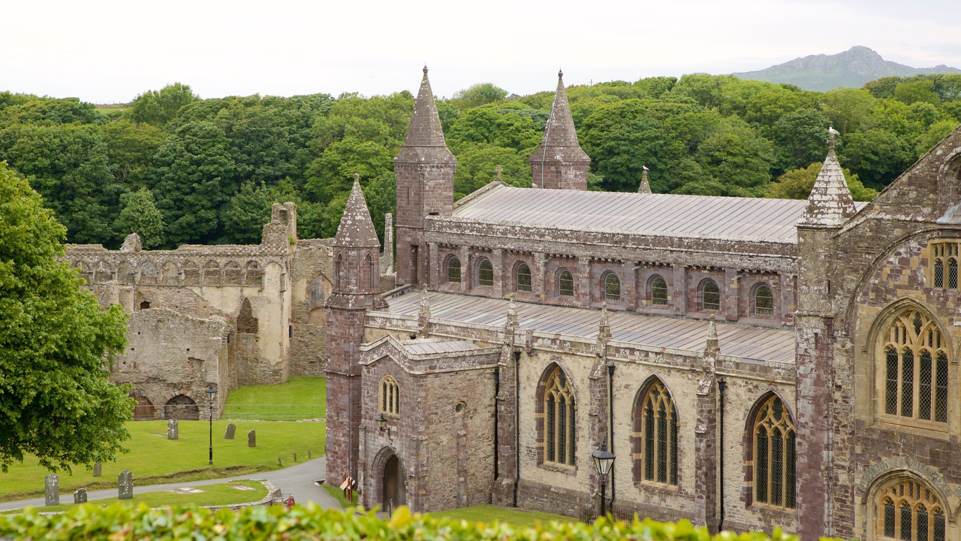 A historic stone building with multiple spires and arched windows, surrounded by lush greenery and a cemetery.