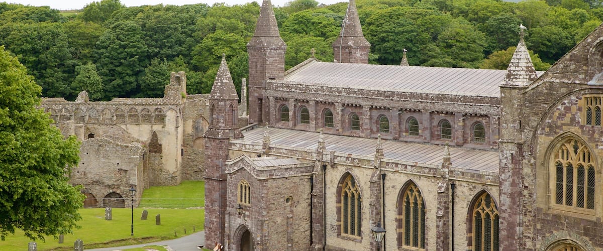 A historic stone building with multiple spires and arched windows, surrounded by lush greenery and a cemetery.
