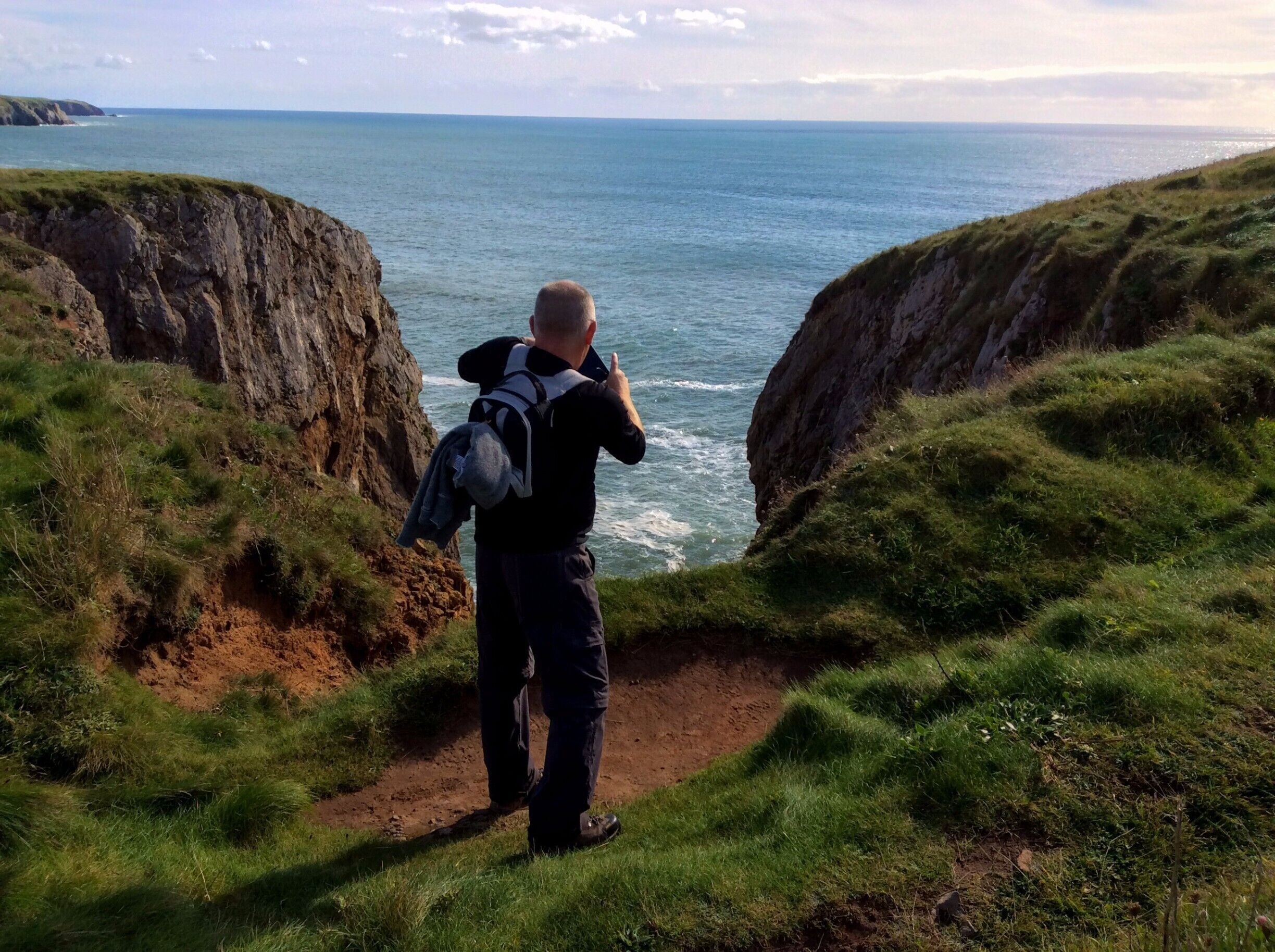 A person taking a photo of a coastal landscape with cliffs and the sea.