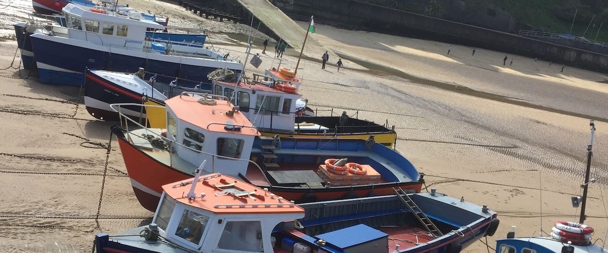 A lone sailor takes the opportunity to clean his boat during low tide on beautiful Tenby harbour beach. The pretty houses in the background are characteristic of this old Welsh town