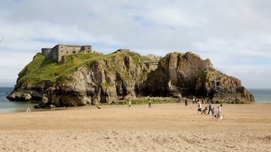 A rocky cliff with a historic building on top and a sandy beach with people.