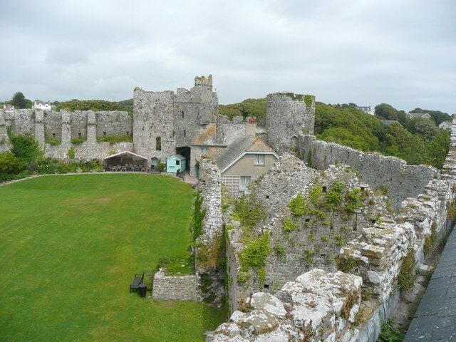 A historic stone castle with a grassy courtyard and a small building in the foreground.